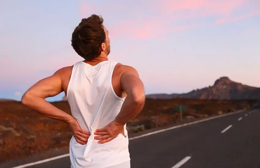 Hombre con dolor lumbar crónico sosteniéndose la espalda durante una caminata al atardecer, representando molestias persistentes en la zona lumbar.